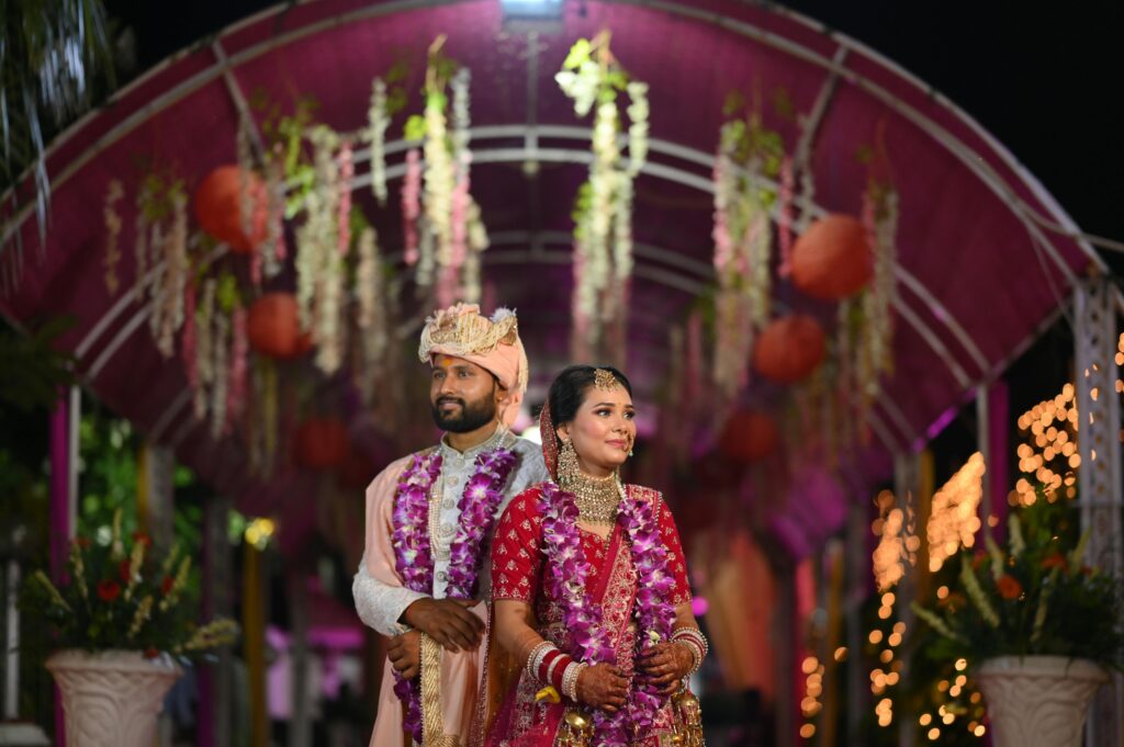 Newlyweds in traditional Indian attire standing under a decorated pavilion at night.