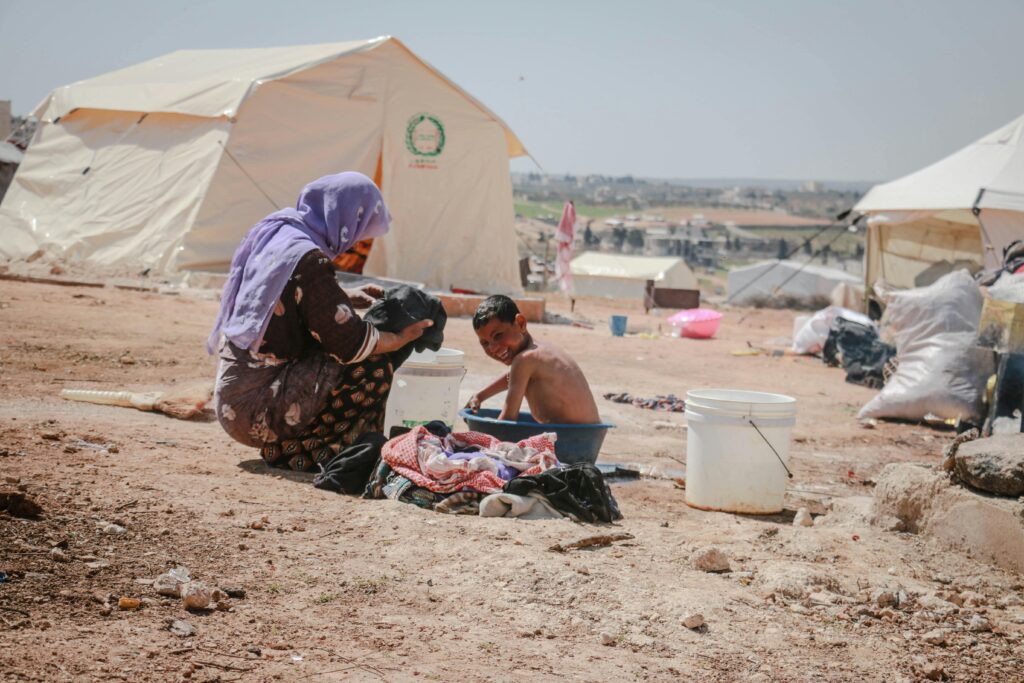 A mother and child washing clothes outdoors in a Syrian refugee camp.