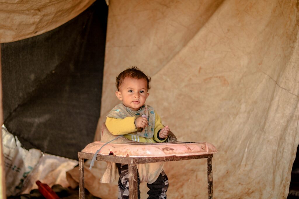 A young child sits in a high chair inside a tent in Idlib, showcasing innocence and resilience.